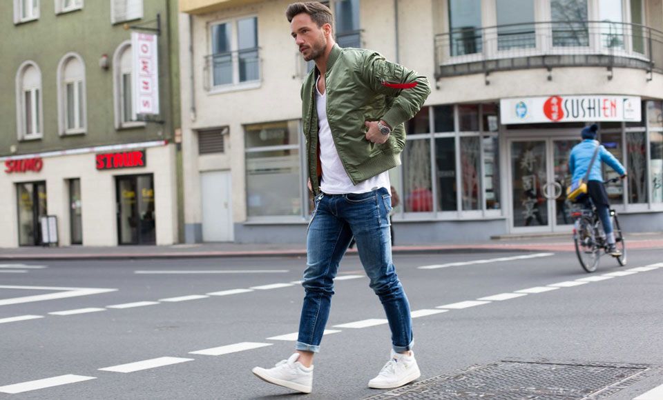 Man wearing a green bomber, white tee, blue skinny jeans and white sneakers.