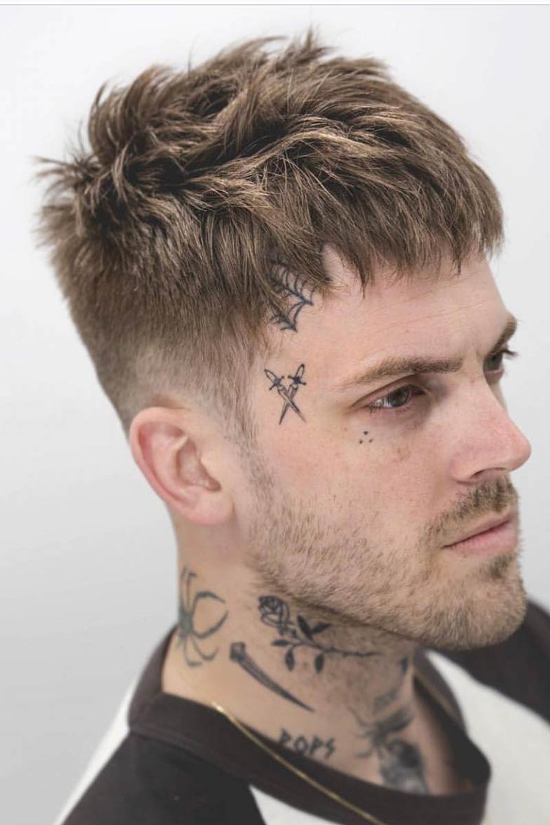 Man with face tattoos and short fringe haircut.
