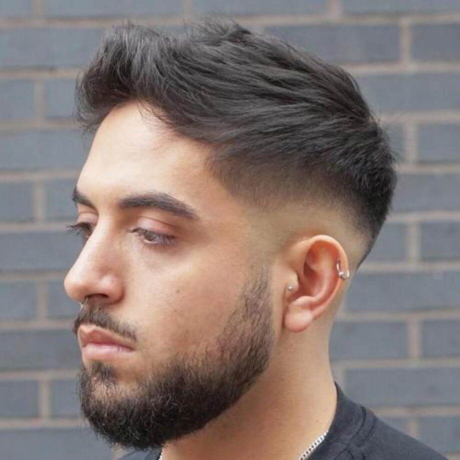 Man with black hair styled in a quiff, with a low fade.