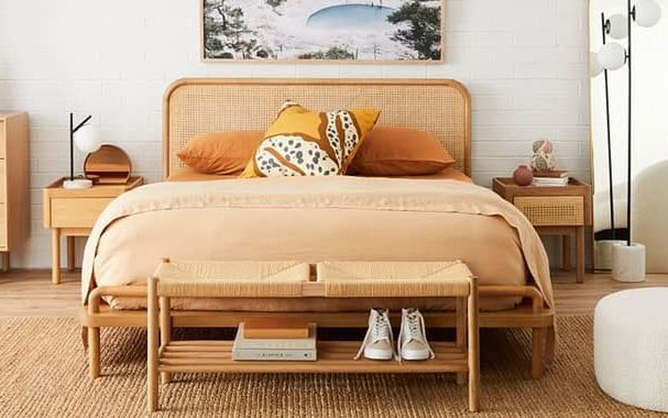 Large Life Interiors bed with coral and orange-coloured bedding. Wooden shoe rack at bottom of bed.