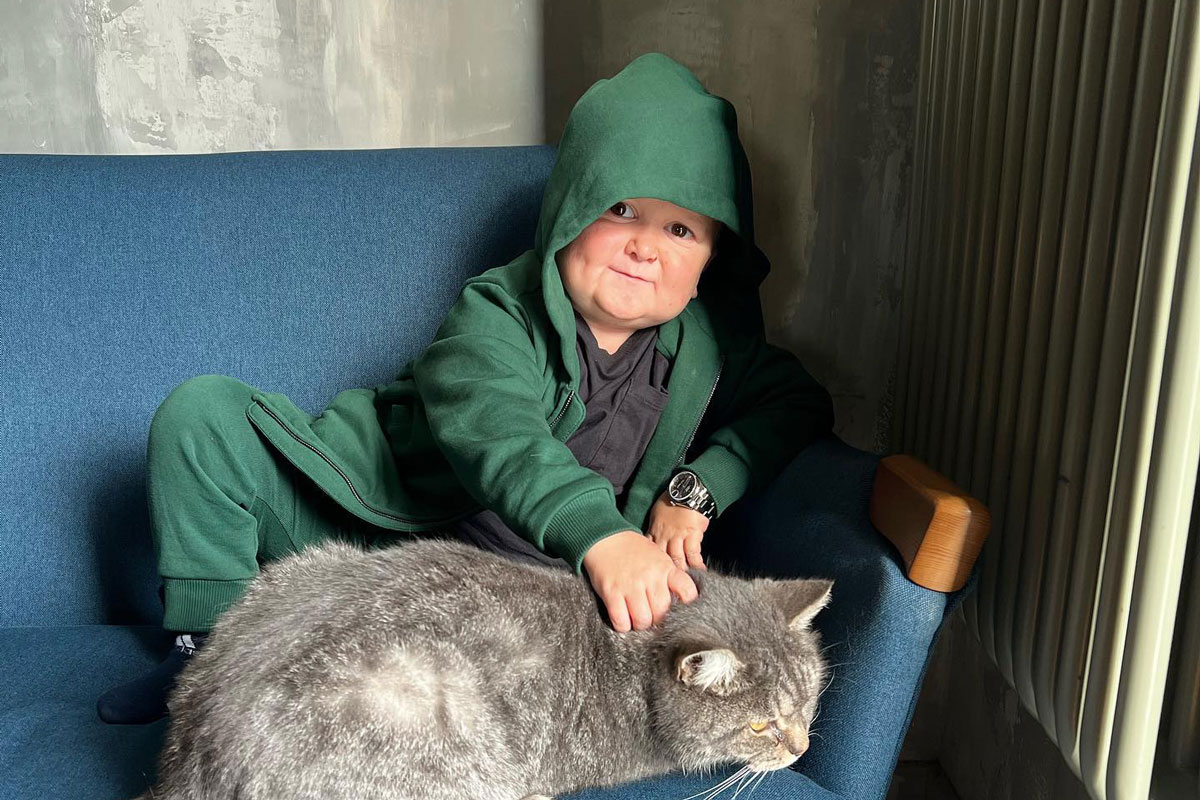 Hasbulla wearing a green hoodie and flash watch, stroking a cat. 
