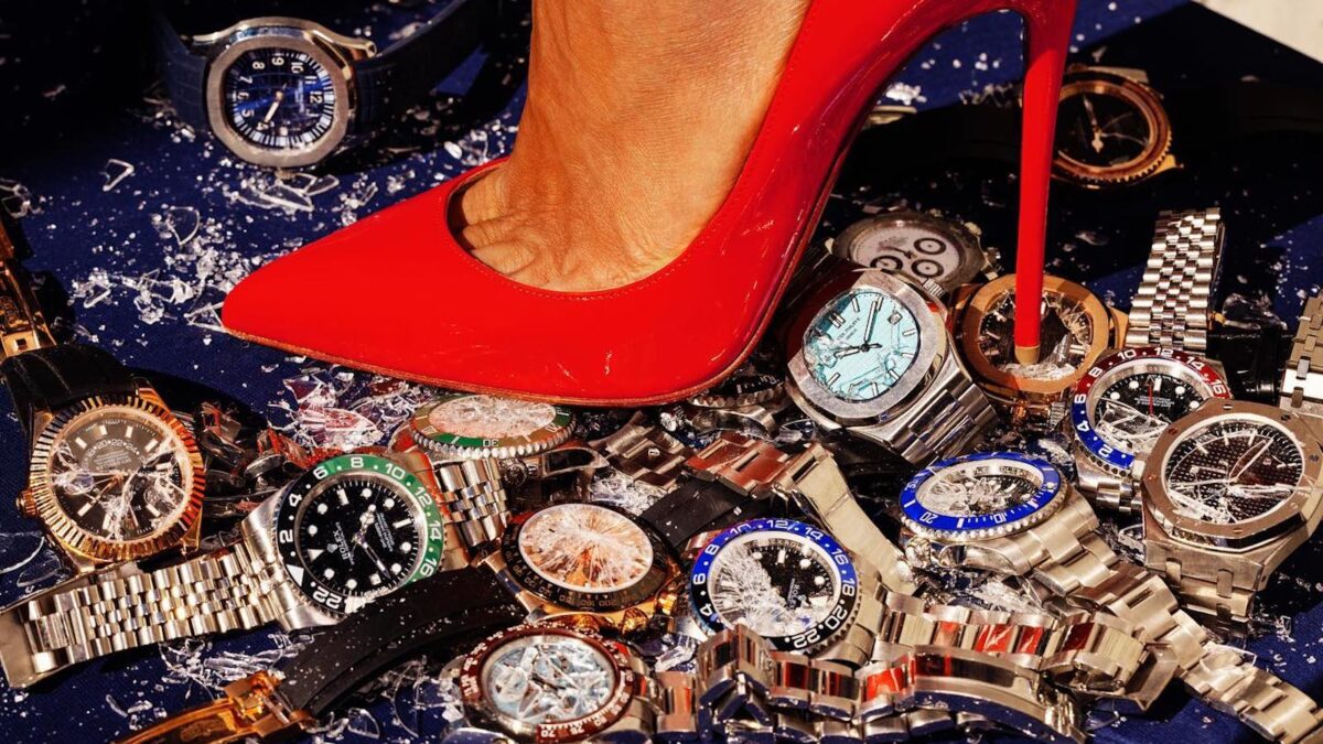 A woman in high heels stomps on a pile of expensive watches.