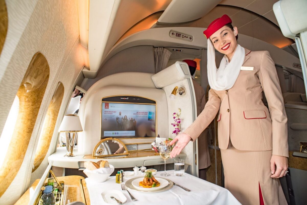 An Emirates flight attendant serving food in first class.