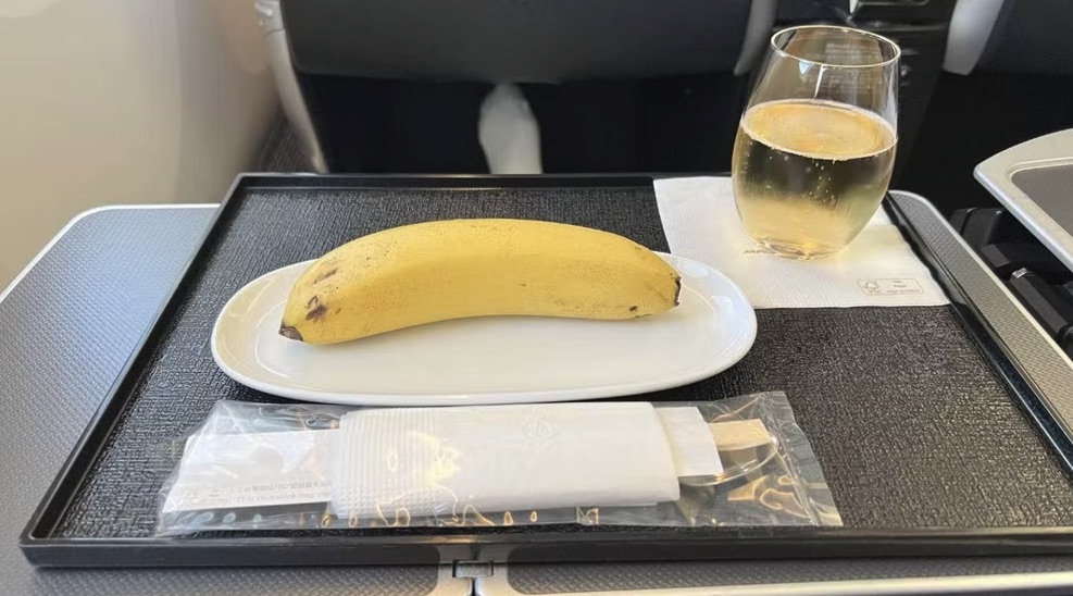 A banana on a plate next to a glass of wine and a set of chopsticks.