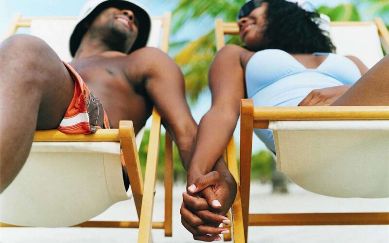 A couple holding hands relaxing on deck chairs.