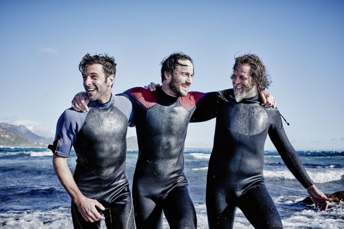 Three men wearing wetsuits and smiling.