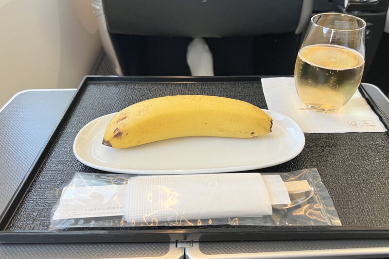A banana on a plate next to a glass of wine and a set of chopsticks.