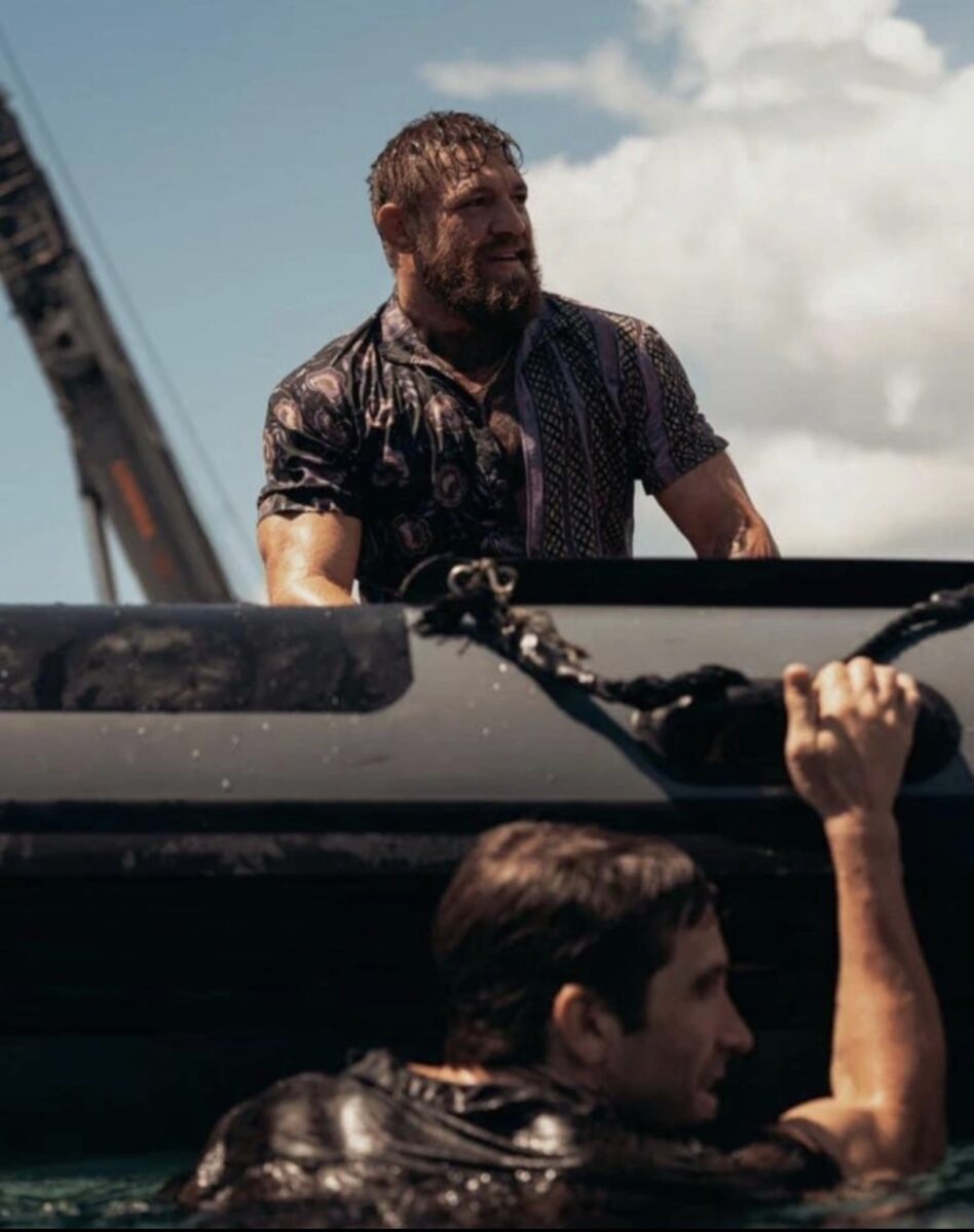 Jake Gyllenhaal hangs off the side of a boat as Conor McGregor watches on.