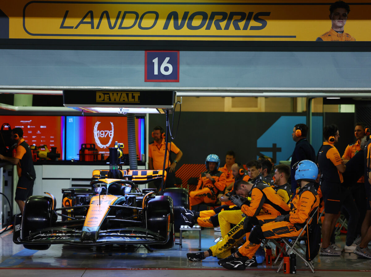 Mechanics sit around a garaged McLaren F1 car.
