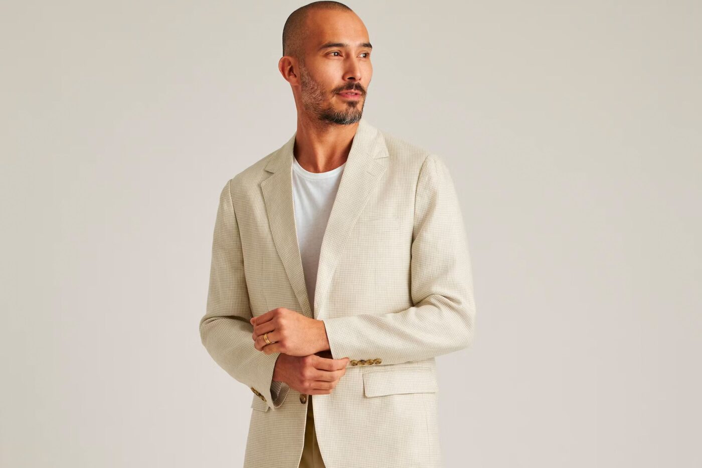 A man wearing an off-white blazer with a white t-shirt underneath, demonstrating a smart-casual look. 