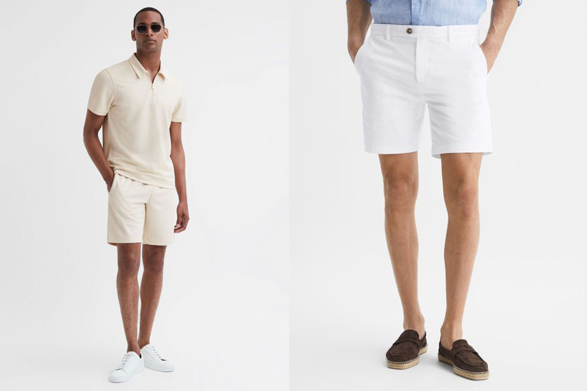 Two mean wearing smart casual outfits with shorts. One wears an off-white polo with off-white shorts. The other wears a blue shirt tucked into white shorts. 