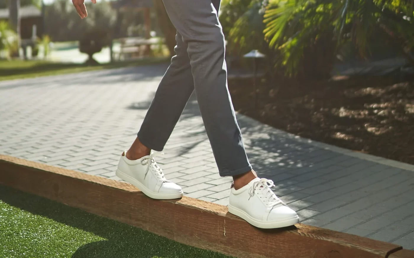 A mean's legs, wearing slim-fit grey chinos and white sneakers.