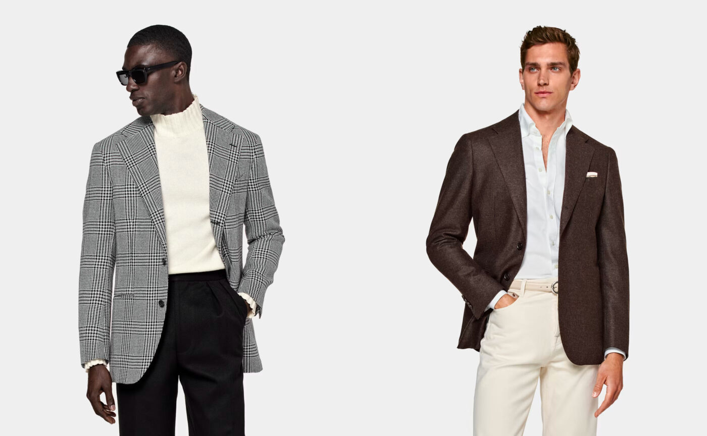 Two men in smart casual clothing. One wears a grey jacket, black trousers, and white turtleneck jumper. The other wears a brown jacket, white shirt, and white trousers. 